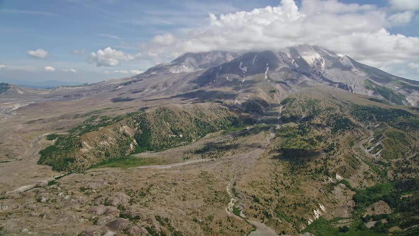 Aerial footage approaching Mount St Helens with clouds capping the peak in Washington's wilderness