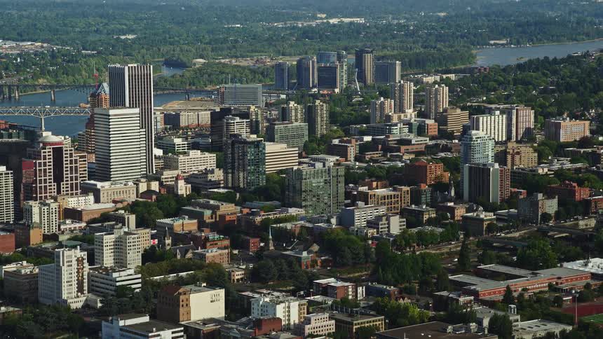  aerial footage capturing the vibrant downtown Portland Oregon with its towering skyscrapers and scenic views of the river and surrounding trees