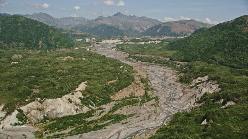Aerial footage of sediment flow in the North Fork Toutle River Washington with sunshine and the river flowing between the forest and the mountains