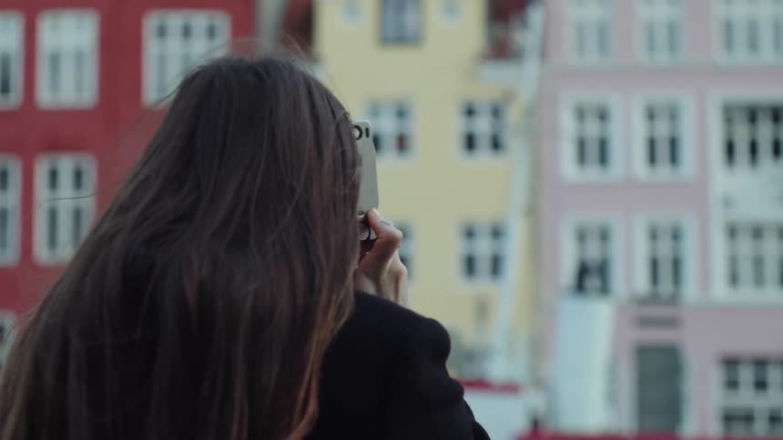 Close up of a woman outdoors during the day holding up a camera and taking a picture of colorful buildings