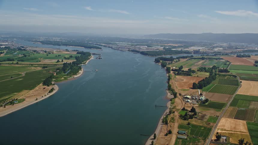 Aerial footage of farmland bordering a wide river with lush green pastures under the sunny daylight captured in the Pacific Northwest region where the Columbia River separates Washington and Oregon