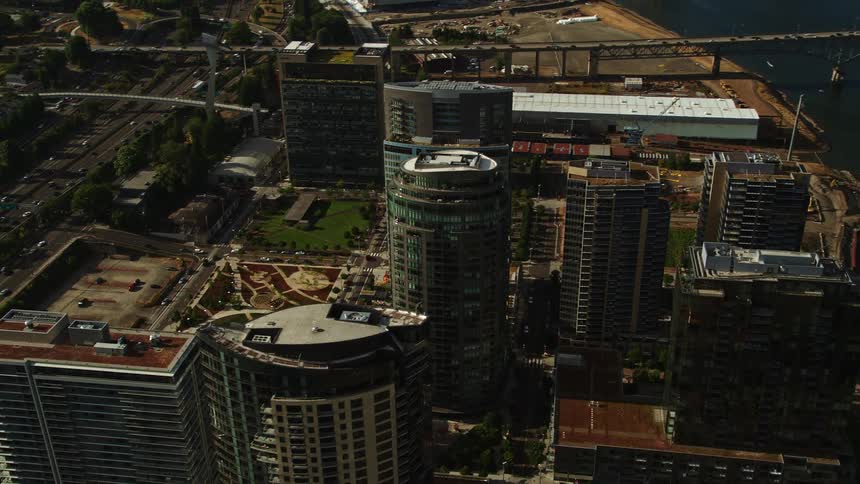 an aerial view of Portland Oregon's South Waterfront neighborhood as the drone flies away from John Ross Tower and The Ardea capturing the modern skyscrapers and beautiful bridges spanning over the Willamette River