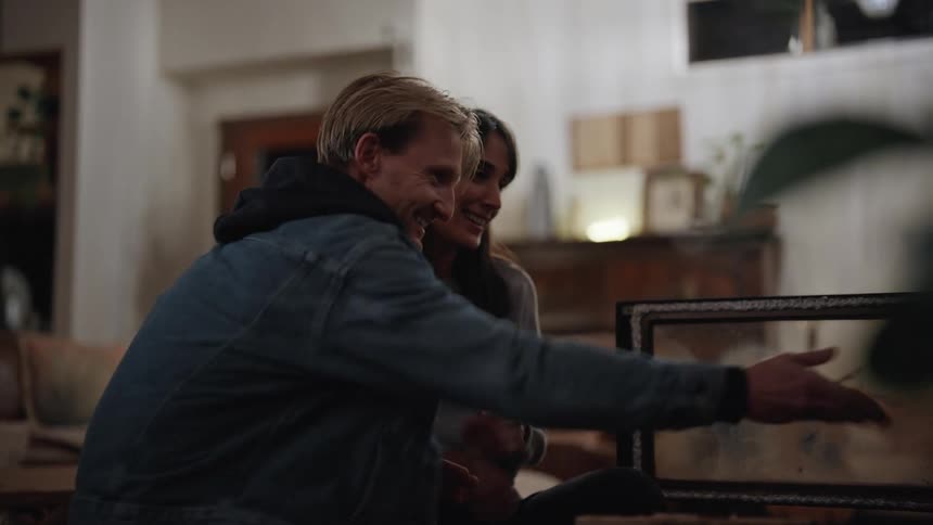 A man and a woman sitting on a couch talk to each other and hug after the man rubs his hands and throws dice on a table
