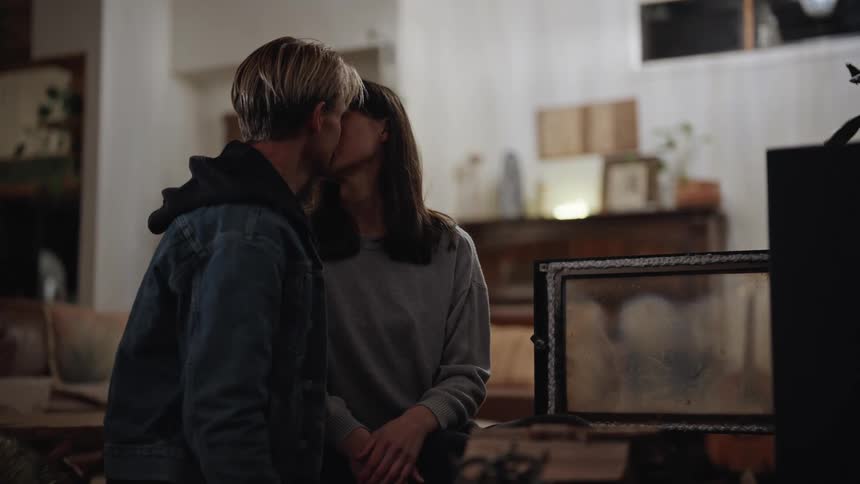 A man and woman affectionately kiss each other while indoors