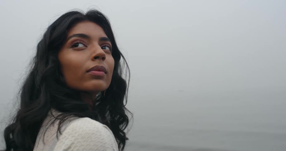 Woman stands outdoor and looks around on foggy windy day