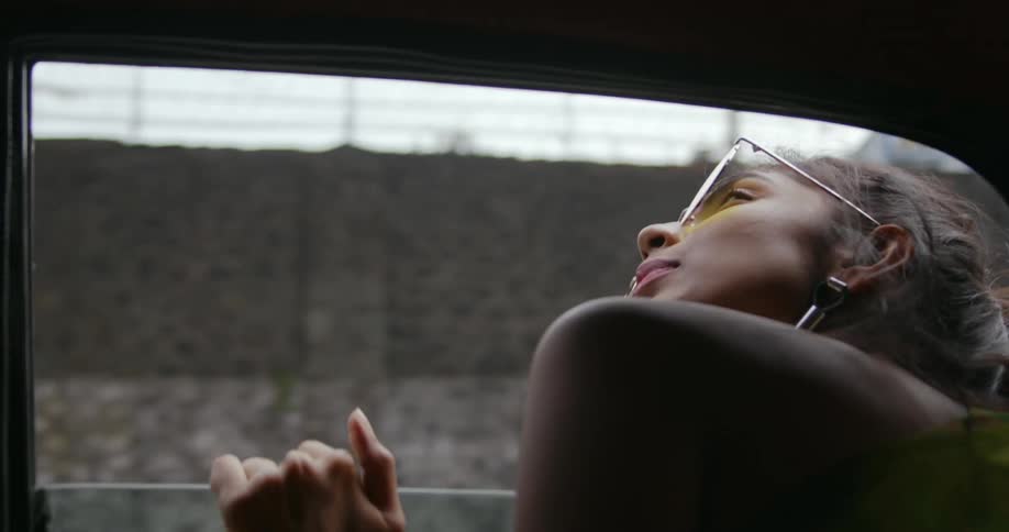 A woman is riding in an automobile as she puts her hands on the window and sticks her head out to look around