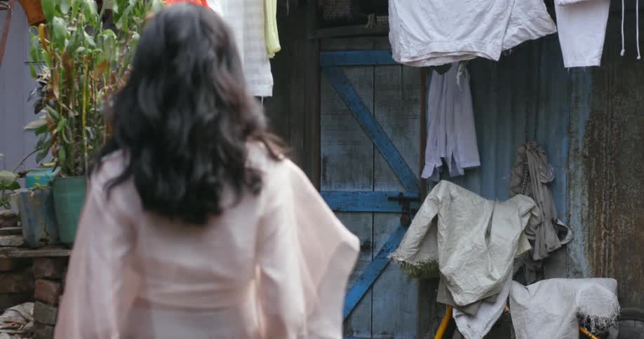 Woman wearing filmy blouse and skirt walks to door past clothes hanging on clothesline