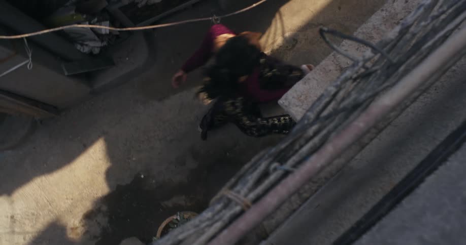 Woman wearing skirt walks down narrow alley between concrete buildings
