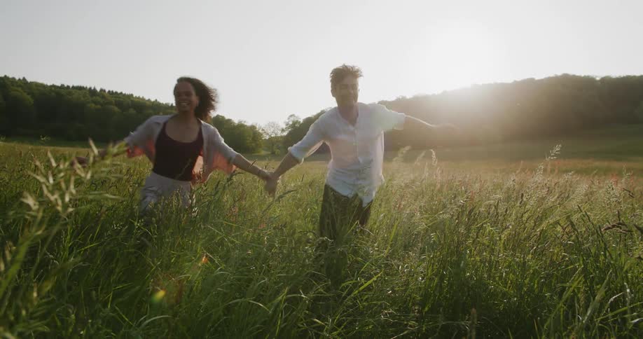 A man and a woman holding hands running and jumping happily in a field of tall plants