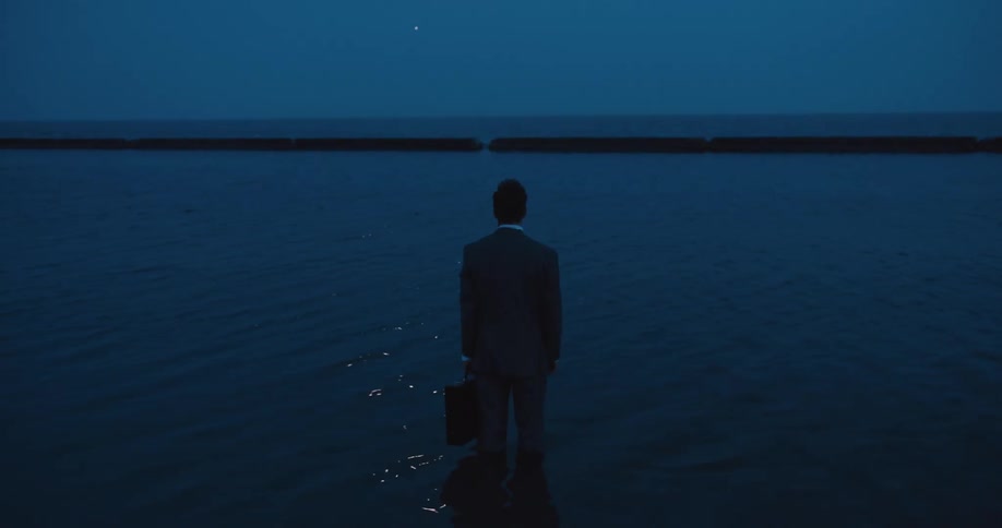 A man in a suit holding a briefcase standing in water at night with the moon reflecting off the surface
