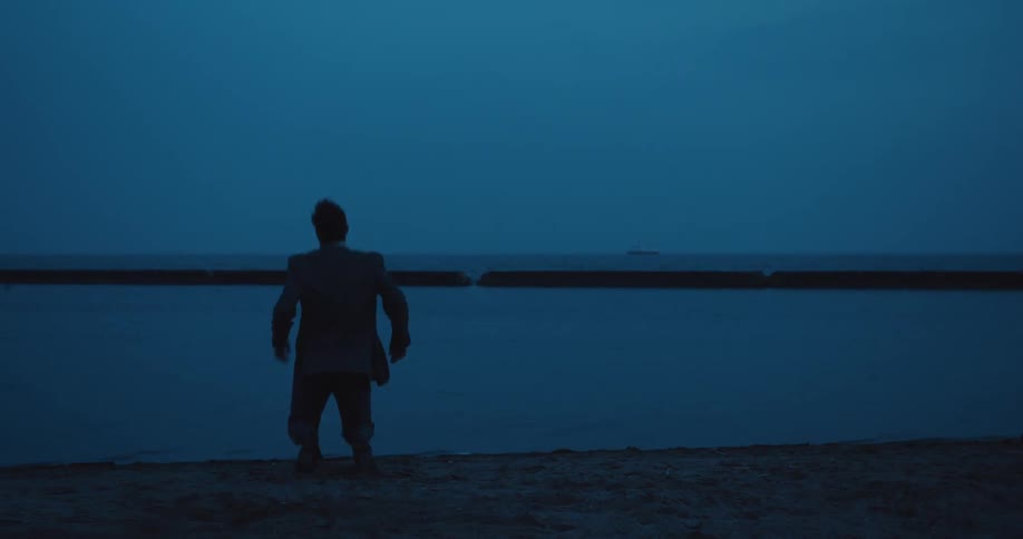 A distraught businessman falls to his knees at the edge of a lake