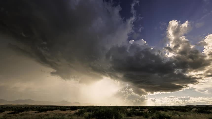 A huge black cloud moving across the sky and blotting out the sunlight that is illuminating the horizon