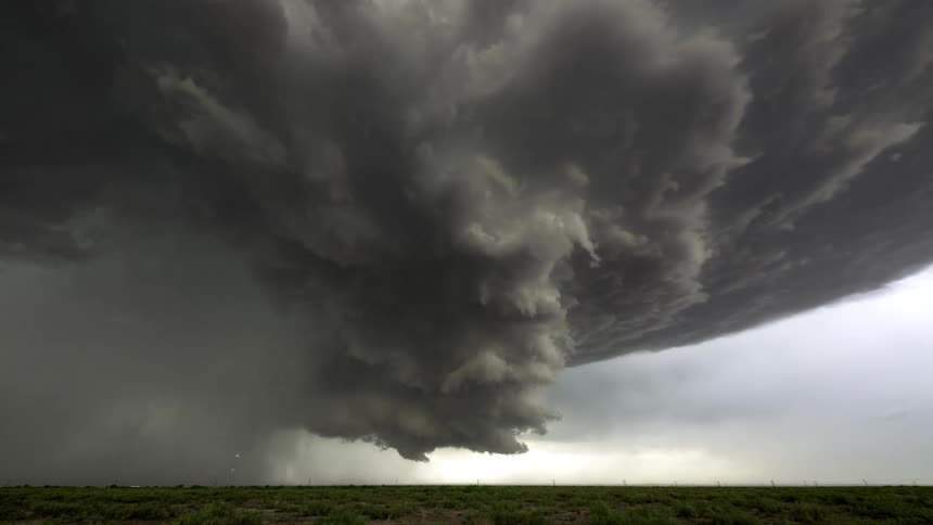 A thunderstorm with dark cumulus clouds forming over a flat grass land during the day as cars travel in the distance