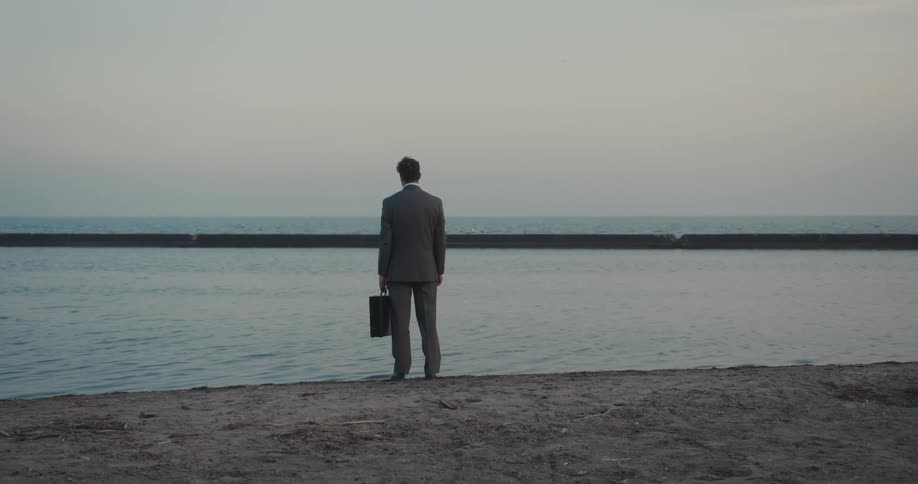 A despondent businessman with a briefcase has an emotional breakdown on the lakeside