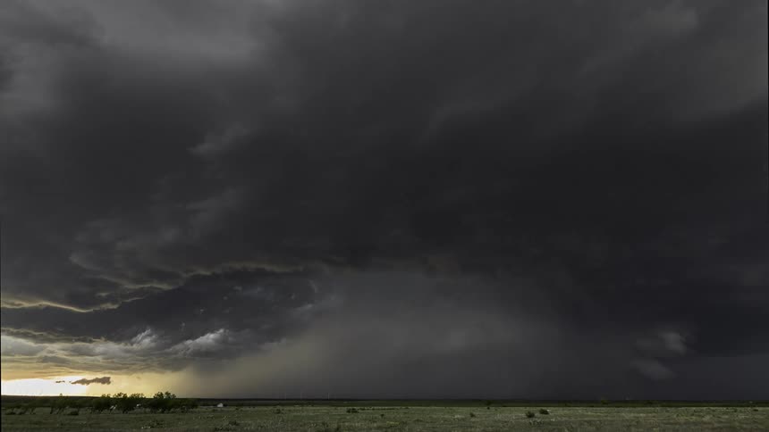 Dark storm clouds rotate while flowing over grassland near farm