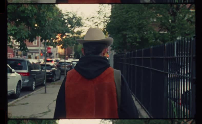 A man in a cowboy hat is walking on a straight sidewalk
