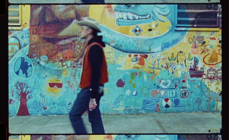 A man in a cowboy hat and orange glasses walking down the street