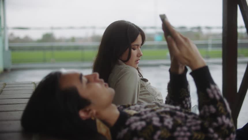 Close up of a man leaning back texting on his phone while a young girl sits next to him talking