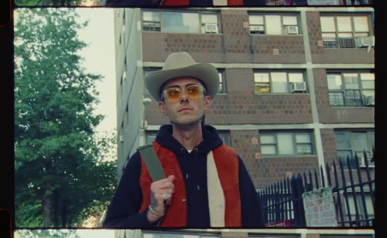 A man in orange glasses and a cowboy hat walks through the suburbs