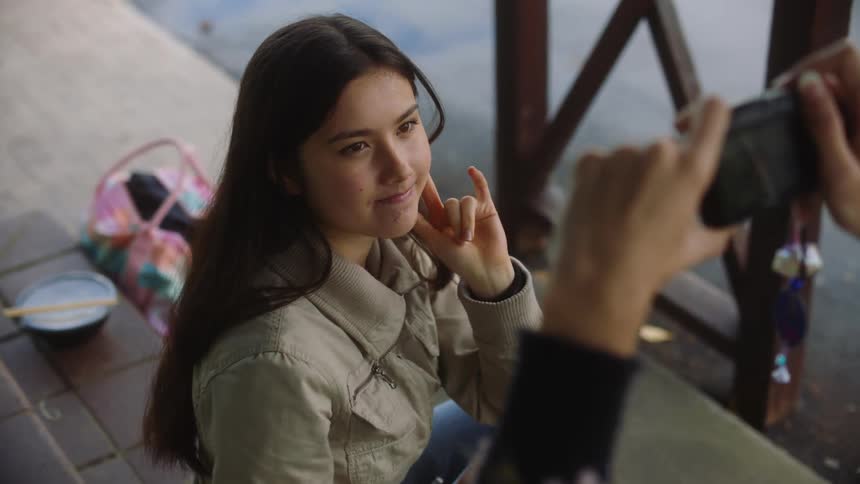Close up of a young girl having her picture taken by a friend while they sit outside