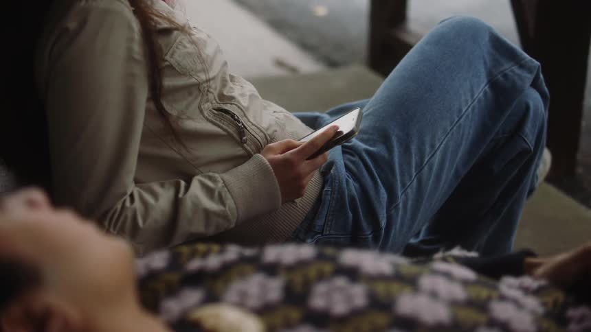 Man talks to woman holding smartphone as they sit near street