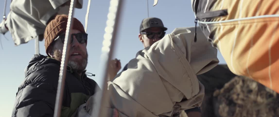 A man picks up a sail while another watches