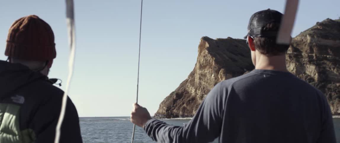 Two men are on a boat looking at a large rock ahead
