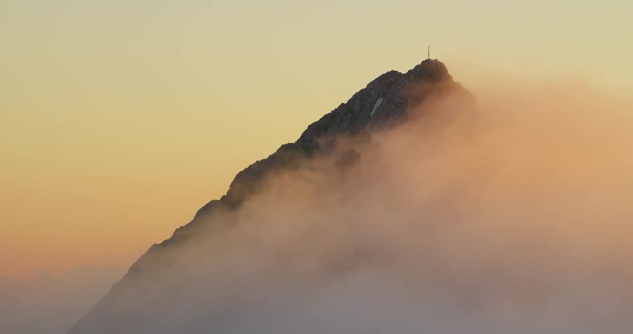 Aerial view of a mountain peak and range covered by clouds during dusk or dawn