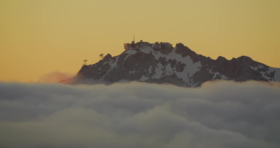 A peak of a mountain above the clouds with snow on top