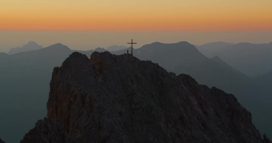 Person stands close to a cross on a mountain top