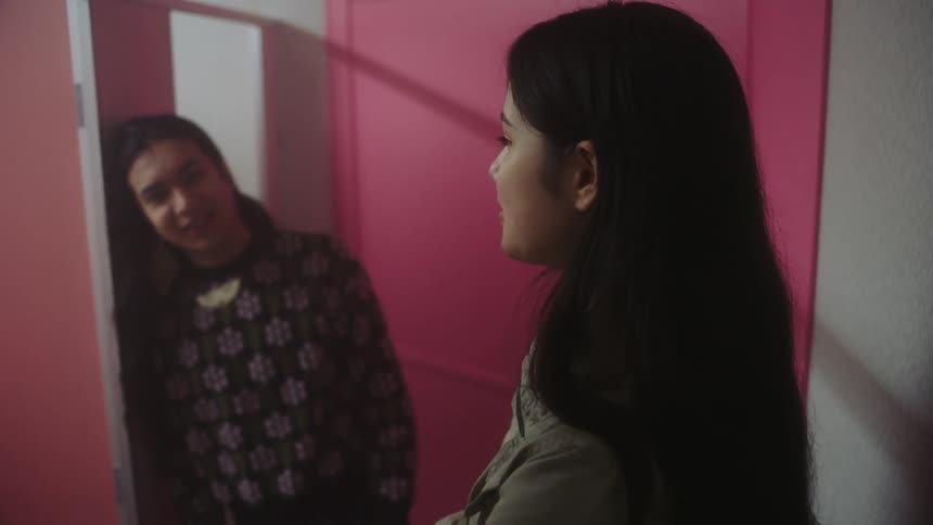Two girls are talking in a closed room with a pink door