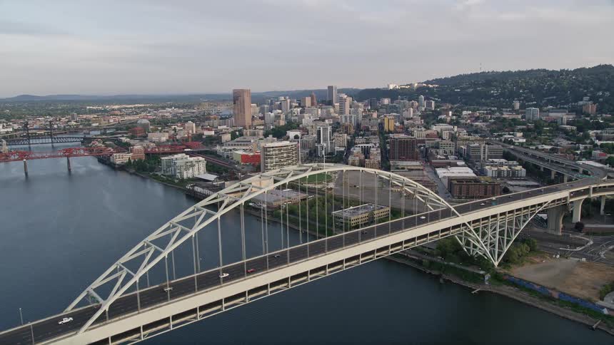 Aerial view of Downtown Portland Oregon at sunset flying over the Fremont Bridge with the American flag waving proudly in the wind