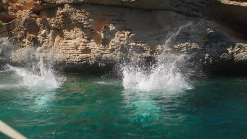 People jumping from a mountain into the blue sea