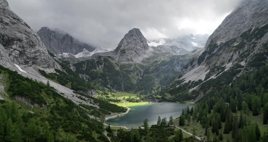 Aerial of a forest with a lake and snowcovered mountains on a cloudy day