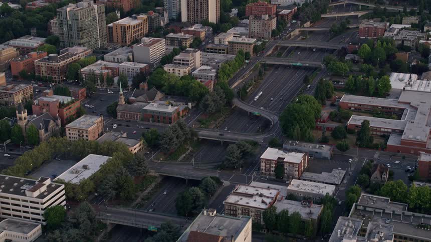 Aerial view of Portland's downtown area during sunset showcasing the busy Interstate 405 with bridges connecting the city's buildings on either side against a backdrop of partly cloudy skies - Pacific Northwest aerial footage