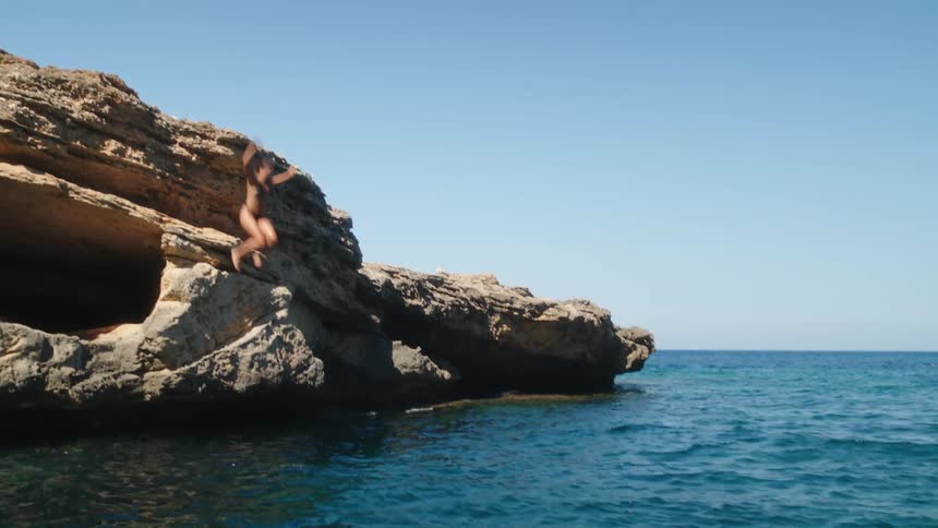 A woman jumps off a huge boulder and lands in the water with a splash
