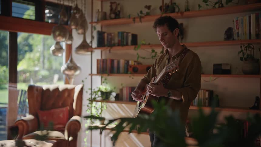 A man playing a guitar while standing close the home library