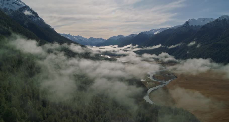 An aerial shot of a cloudy mountain range and wilderness