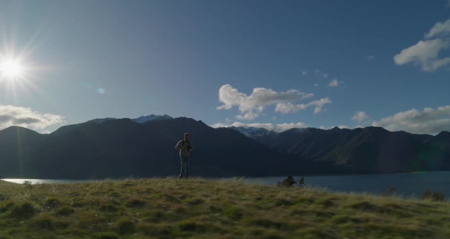 Man walks across grass near mountains and lake on a sunny day
