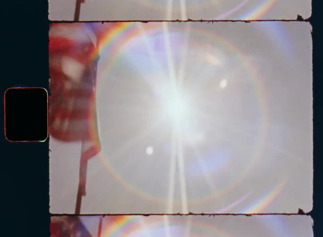 The American national flag is moving and waving on a flagpole in the wind on 4th of July a bright sunny day with blue sky celebrating the independent United States of America on vintage Super 8mm film with lens flare
