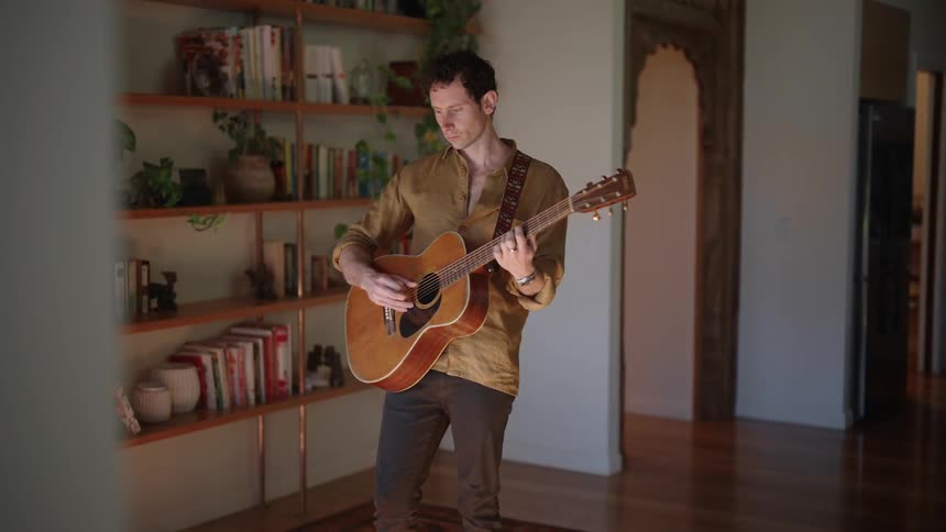 Young man plays acoustic guitar in the middle of the living room at home