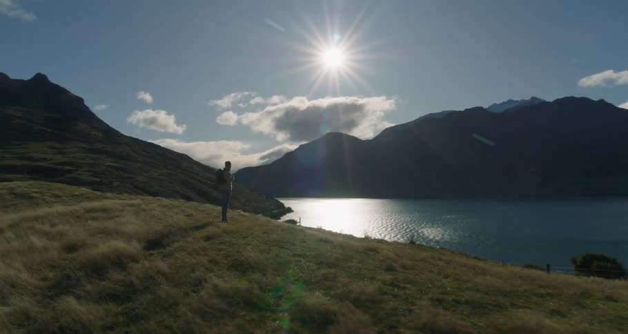 An adult hiker stands on a grassy knoll overlooking a mountain lake