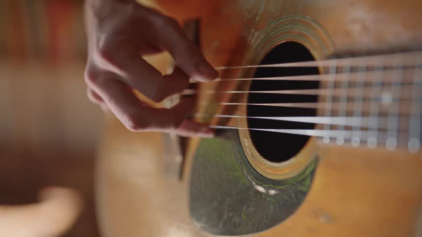 A human hand plucking the strings of an acoustic guitar with the fingers