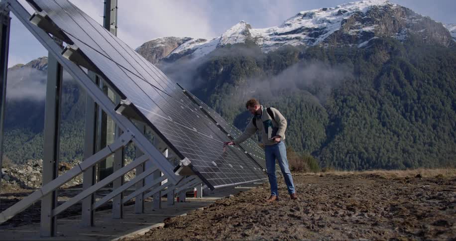Man holding his laptop and checking the solar panels of energy located near the mountains