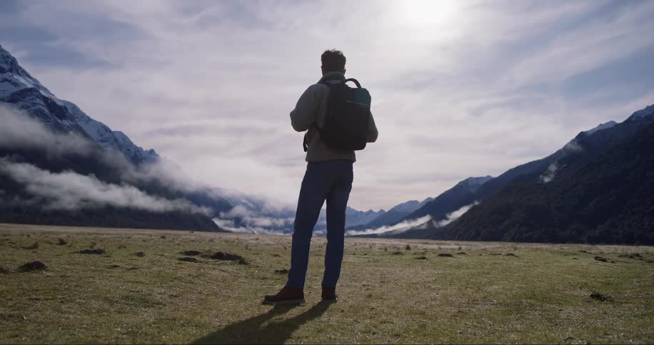 Man carrying a backpack stands on a valley near the mountains