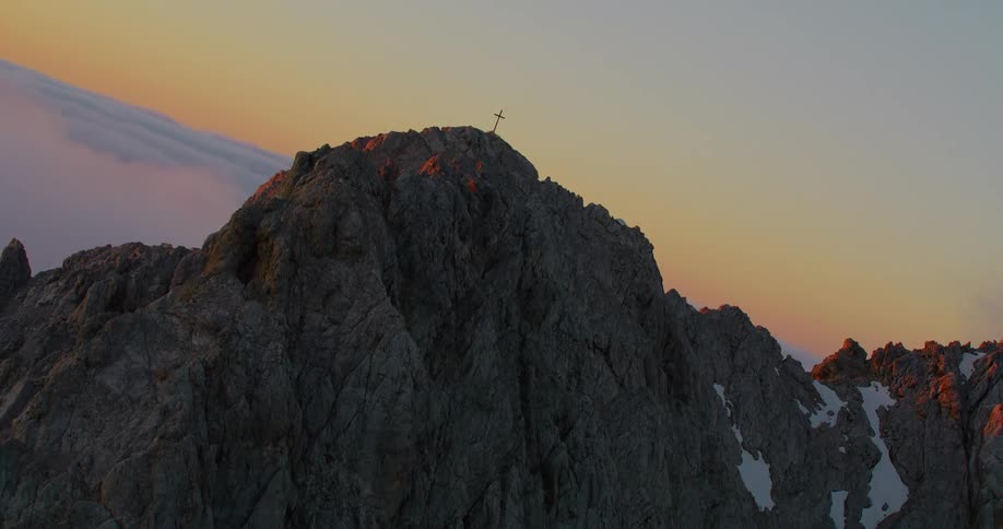 Aerial of a cross on the peak of a mountain range at sunset
