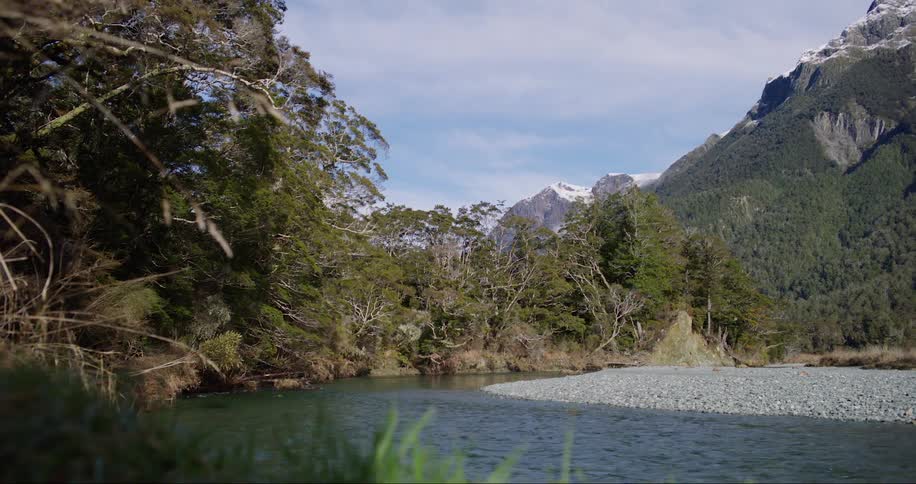 River flowing near the forest with high mountain range in the background
