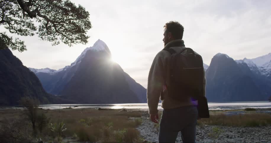 A man in a sweatshirt and backpack stands looking out at distant mountain peaks
