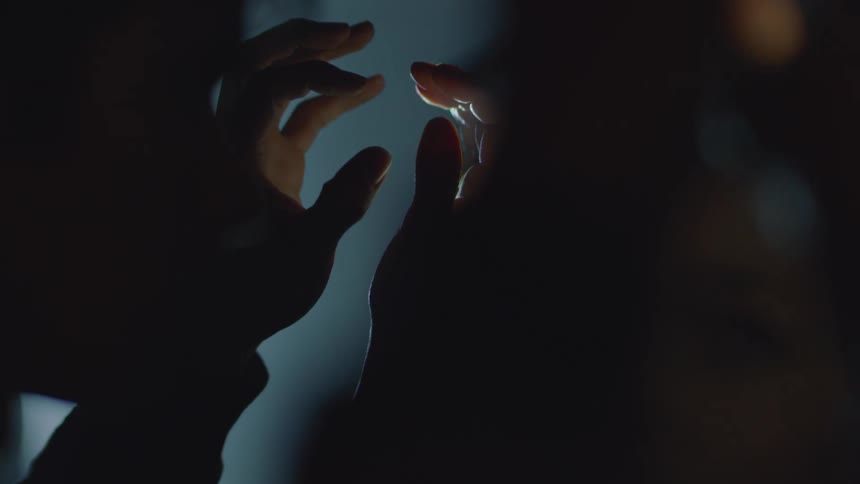 Male person indoors playing with their hands against the light of a projector