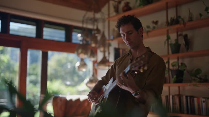Young man plays acoustic guitar in the middle of the living room at home